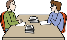 2 Personen sitzen am Tisch und sprechen miteinander.