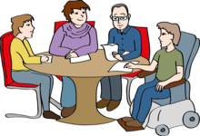 4 Prüfer sitzen an einem runden Tisch. Sie unterhalten sich und prüfen Texte.